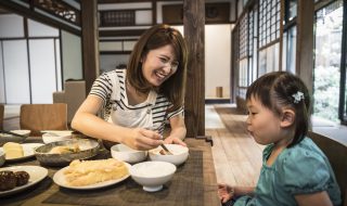 Young Japanese girl sitting at table with mother eating dinner, mother smiling, daughter watching